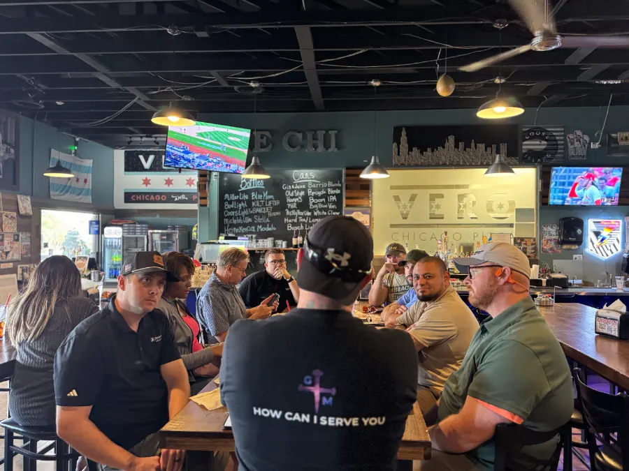 A TPC leader in a How Can I Serve You shirt addressing members at Vero Chicago Pizza